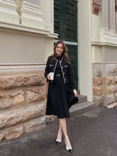 A lady wears a tweed jacket and a pleated dress.